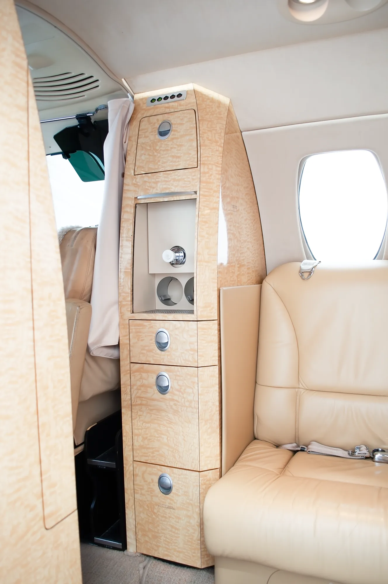 A close-up view of light wood cabinetry and a tan leather seat in the aircraft's cabin interior.