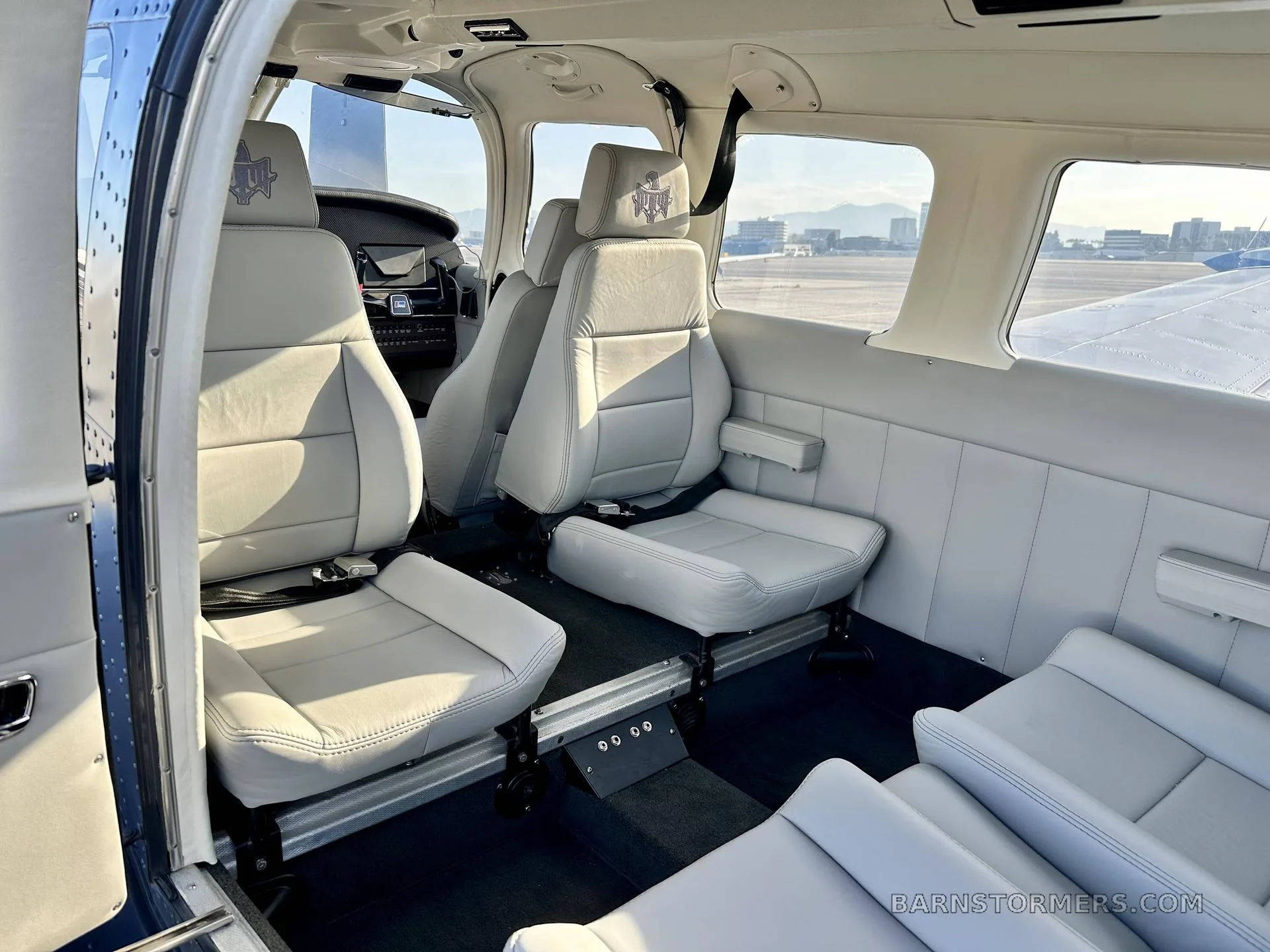 The light gray leather interior cabin of an aircraft with four seats visible, featuring headrests with an emblem.