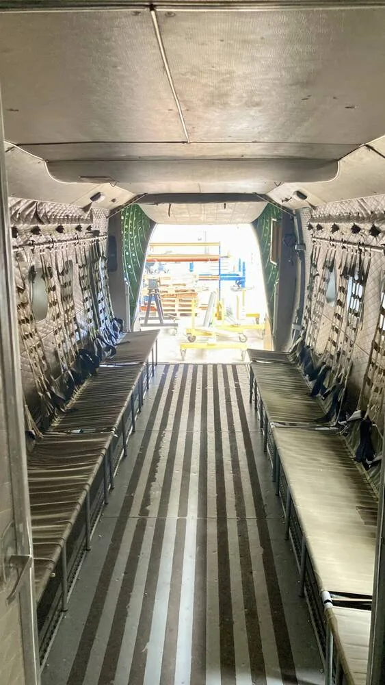 The spacious interior of a military transport aircraft's cargo hold with benches and a view out the rear ramp.