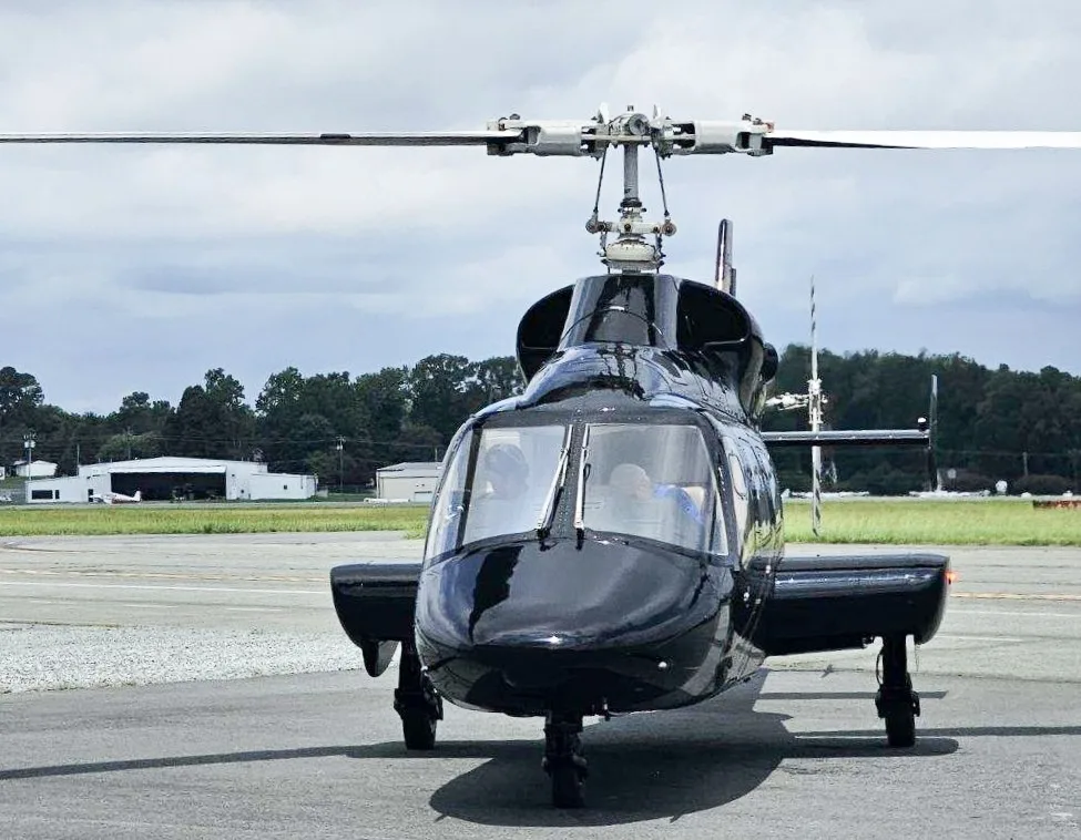 Front view of a black Bell 430 helicopter with gold stripes on an airfield.