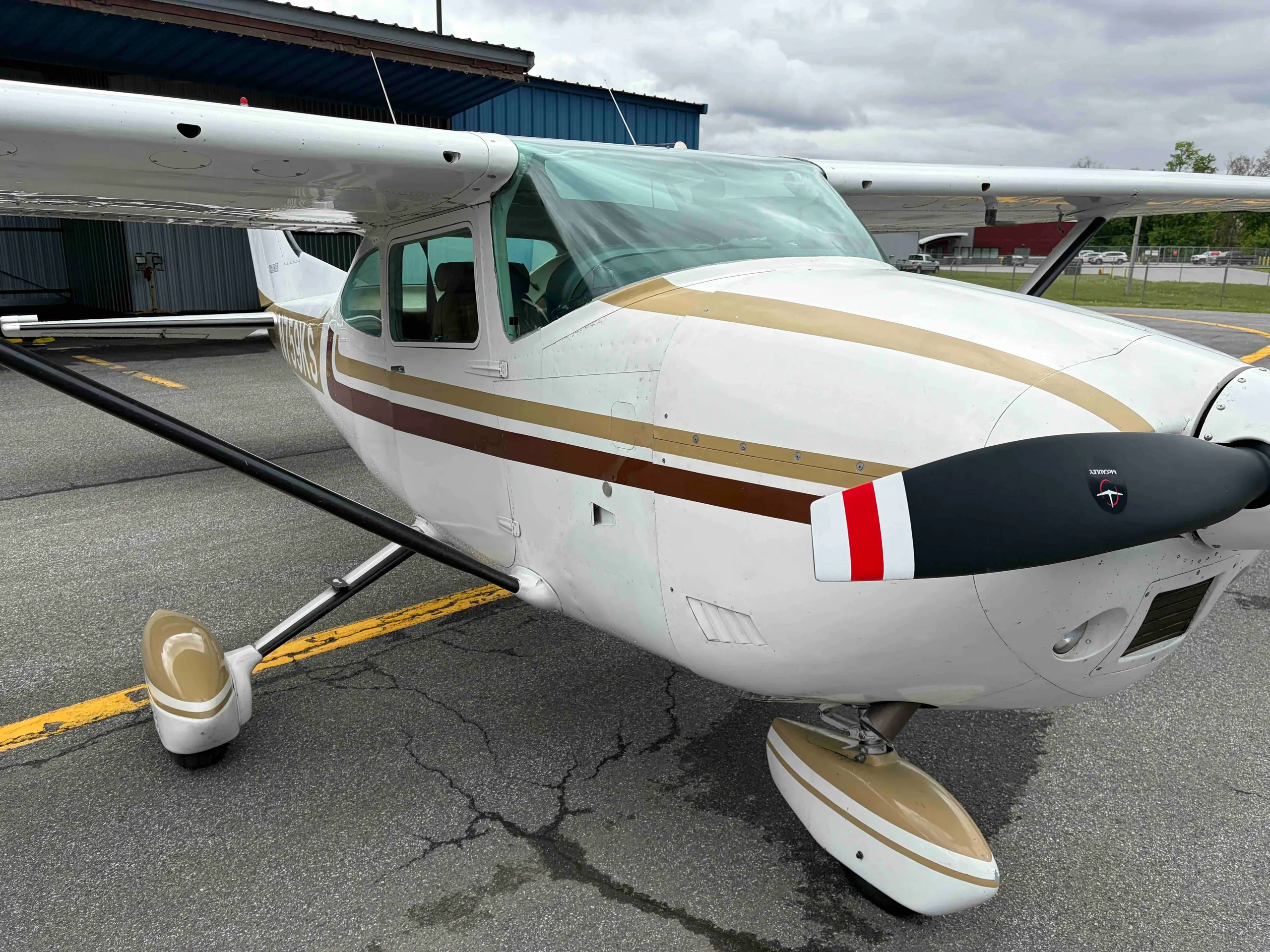 A close-up front view of the white Cessna 182 Skylane N759KS, showing the propeller and nose with red and white stripe.
