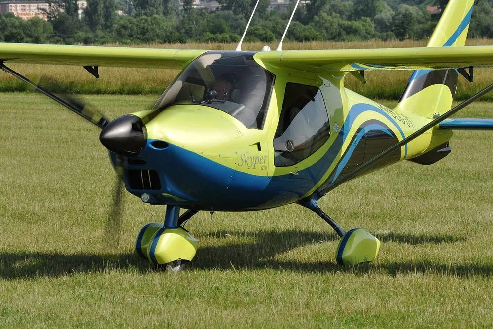 A yellow and blue Skyper GT9 ultralight aircraft with a propeller on a grassy airfield.