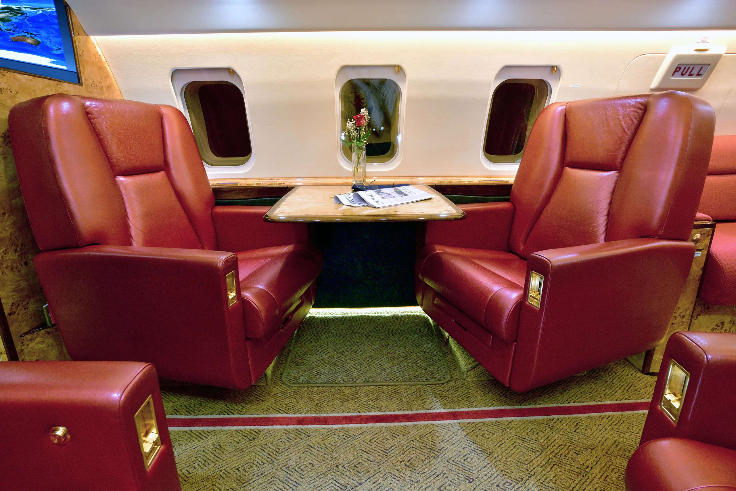 A close-up view of two red leather seats facing each other with a wooden table between them in a private jet cabin.