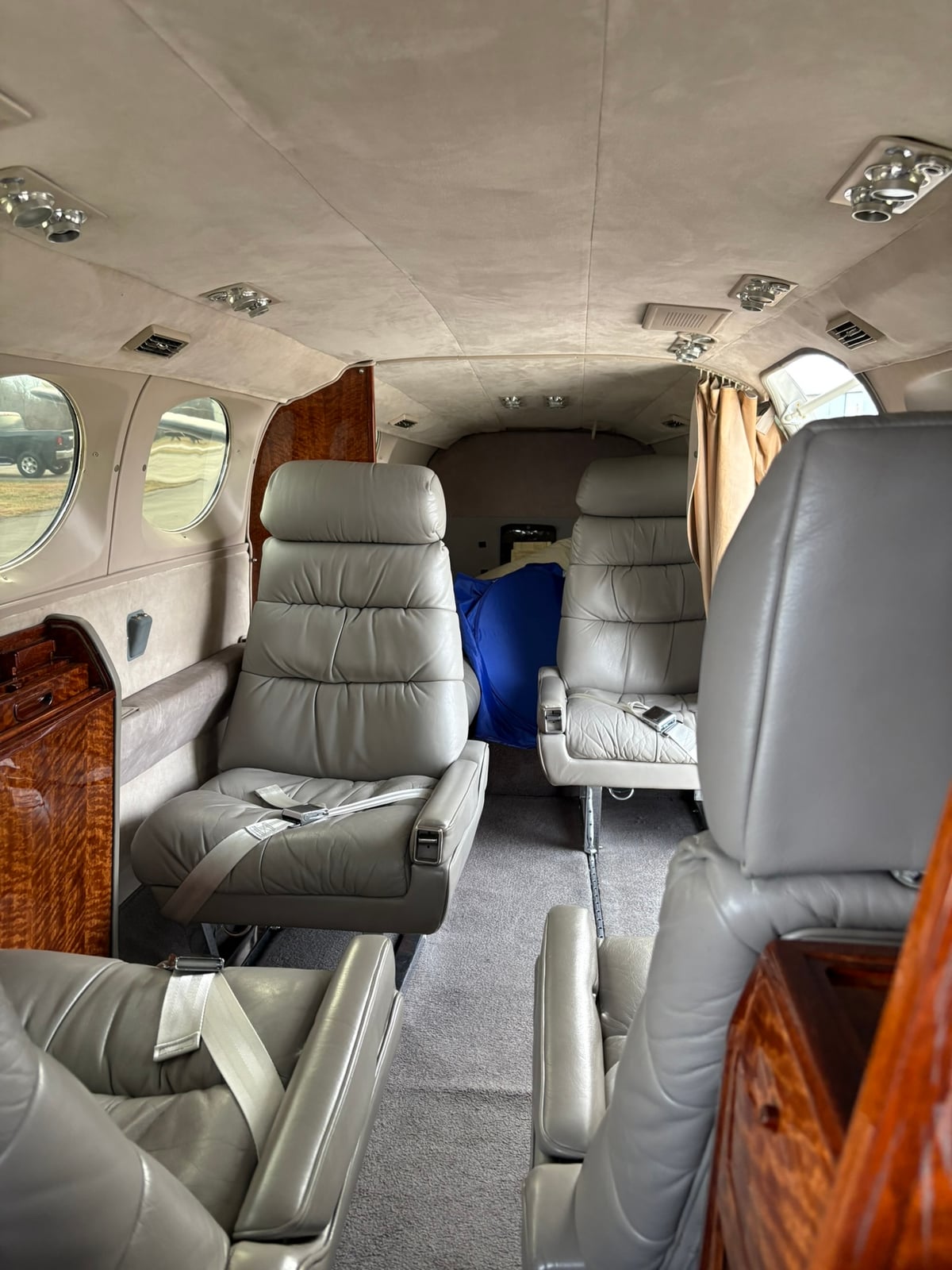 View of the aircraft cabin interior with grey leather seats and wood paneling.