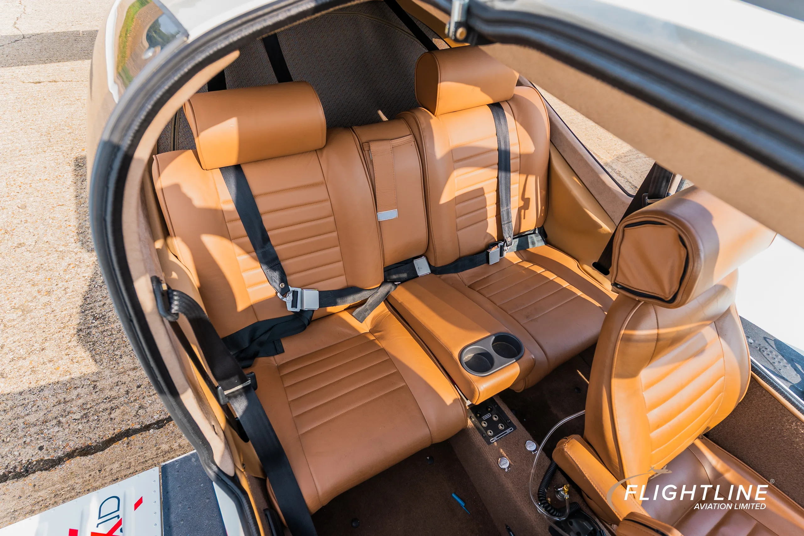 An overhead view of the N377C Socata Trinidad GT's rear cabin, showing two tan leather seats with seatbelts and a center console.