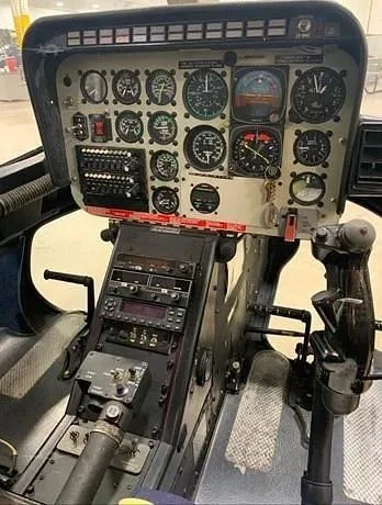 The cockpit instrument panel of a helicopter, featuring various gauges, switches, and flight controls.