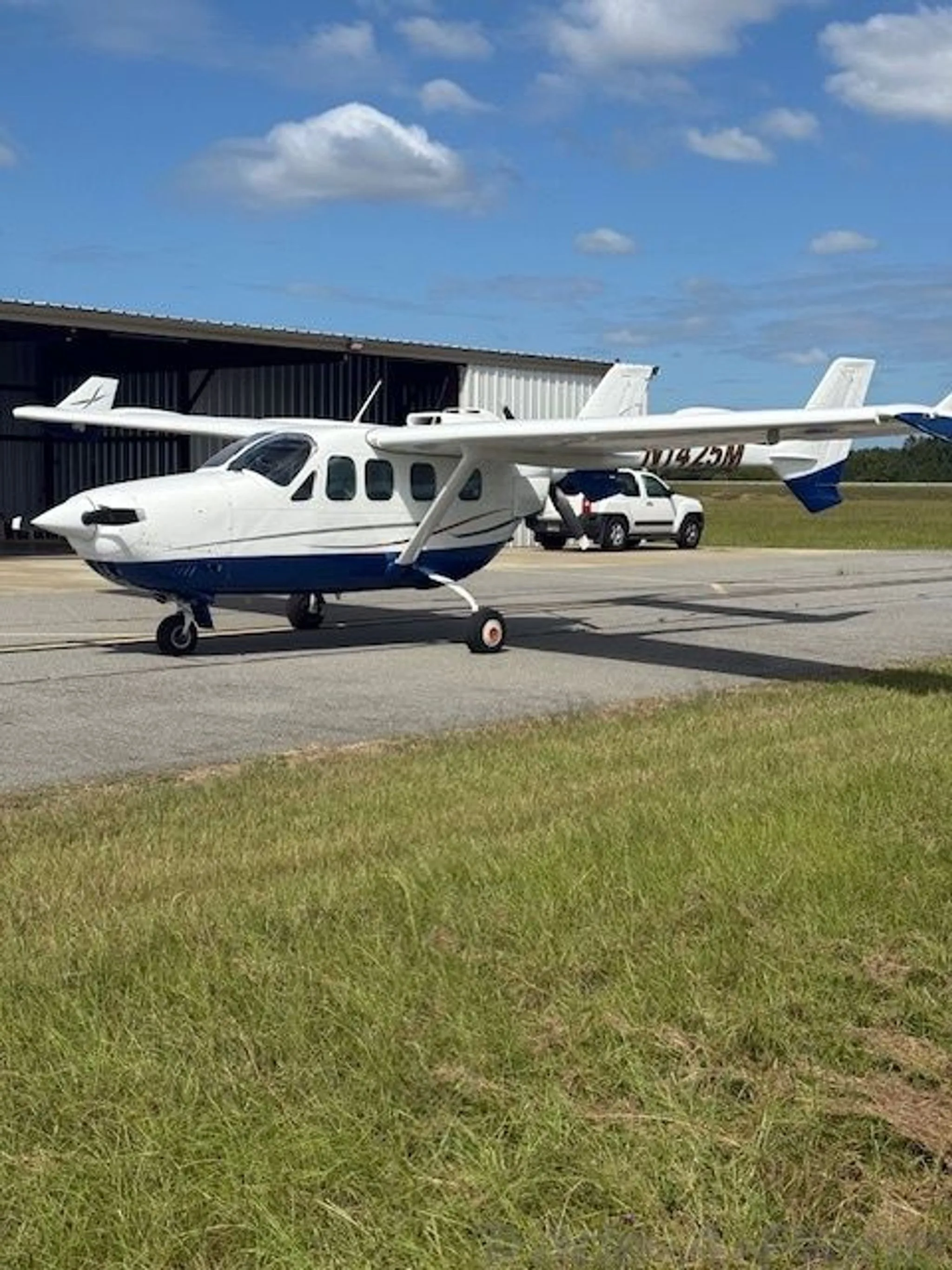 A white and blue Cessna 337 Skymaster aircraft, N1425M, parked on a tarmac next to a hangar.