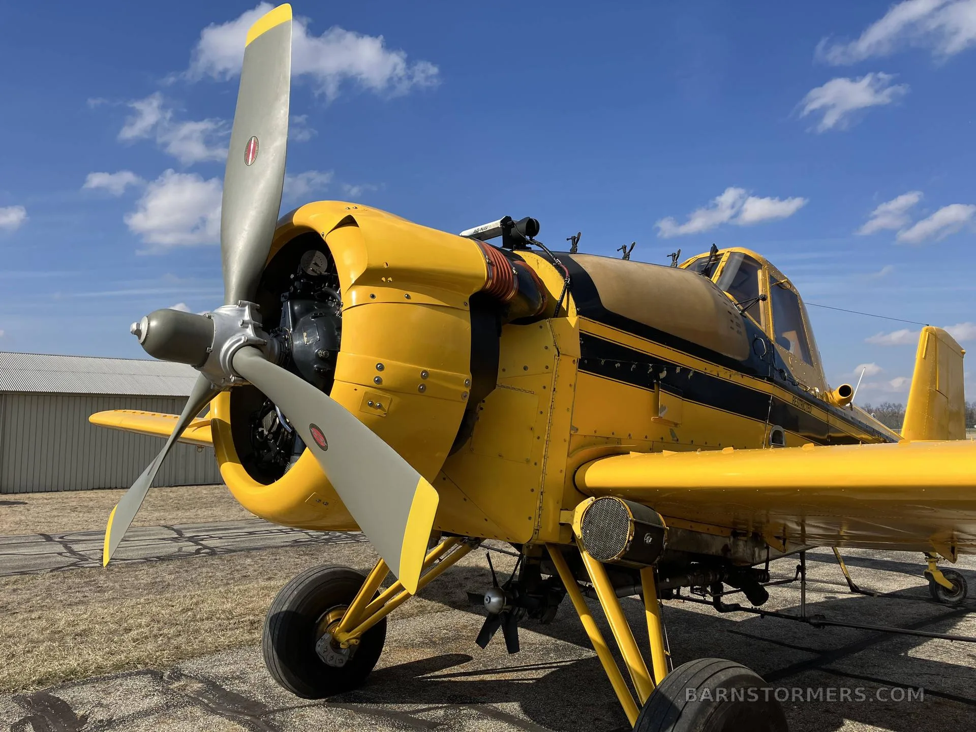 A close-up view of the front and right side of a yellow agricultural aircraft, showing the propeller and engine cowling.