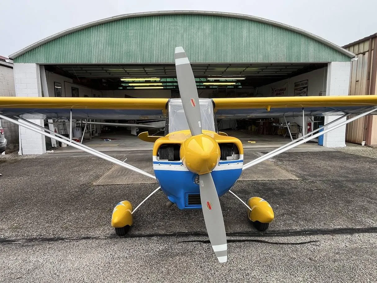 A head-on view of the yellow and blue Super Decathlon aircraft with tail number N71SD, parked in front of an open hangar.