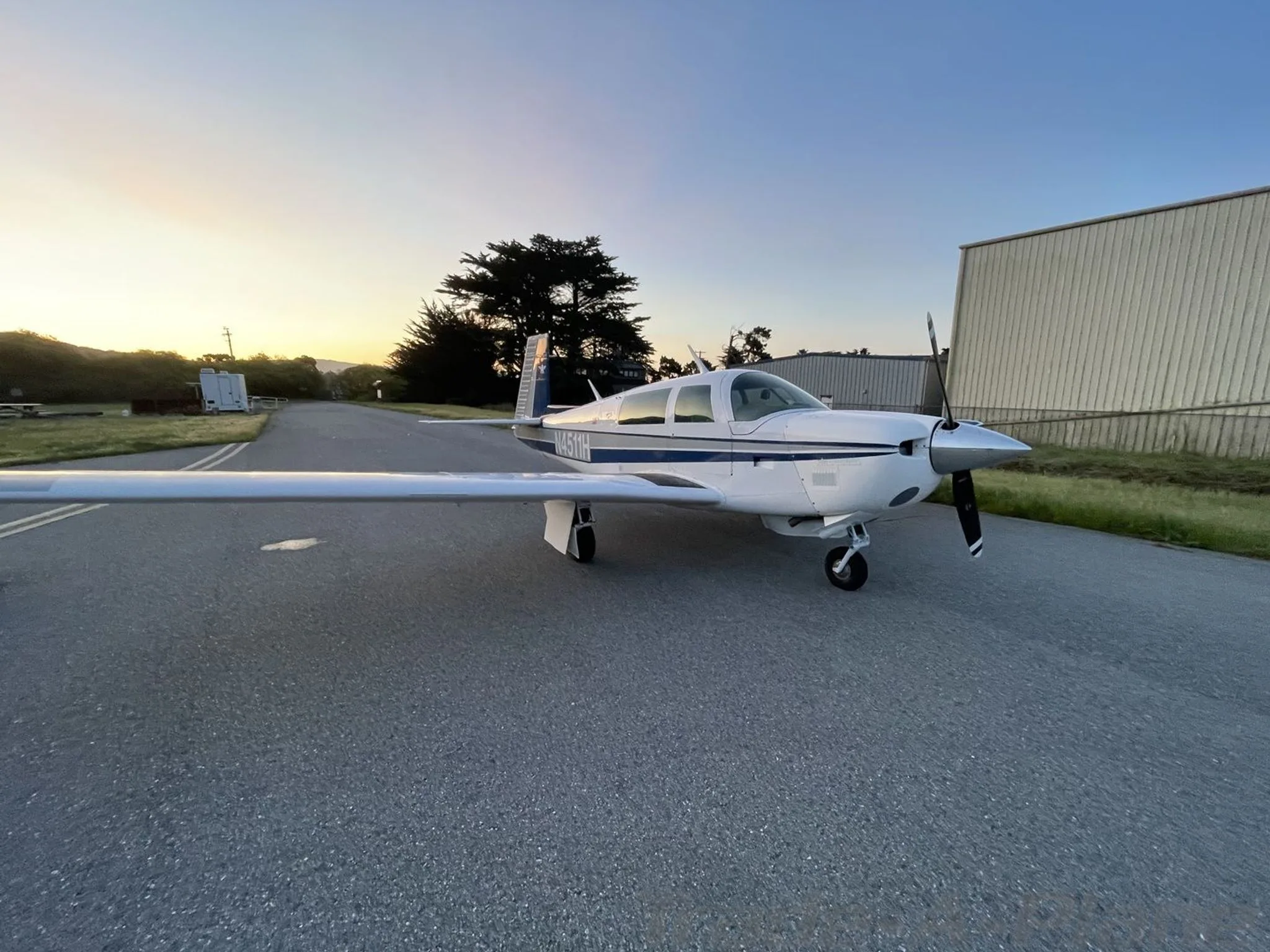 A white and blue single-engine aircraft, N4511H, parked on an asphalt ramp at sunset.