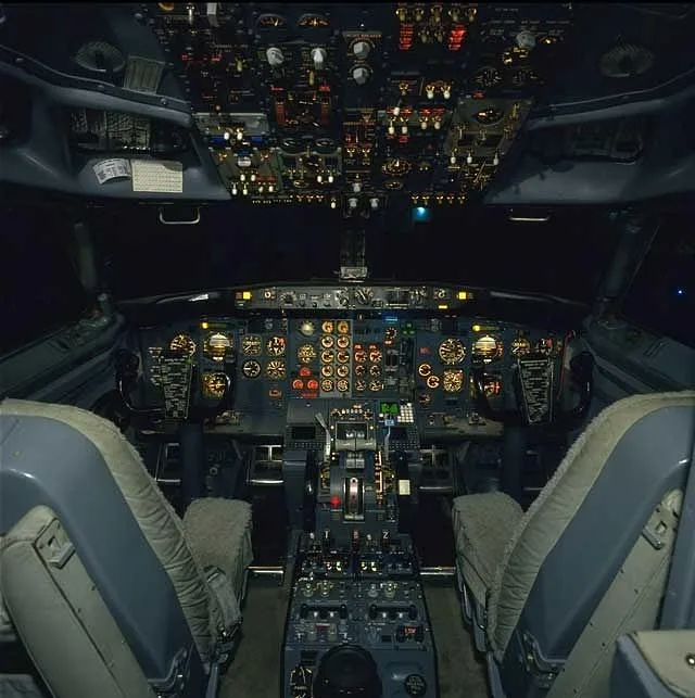 The illuminated cockpit of a Boeing 737 features numerous dials, switches, and controls on the instrument panel and overhead console.