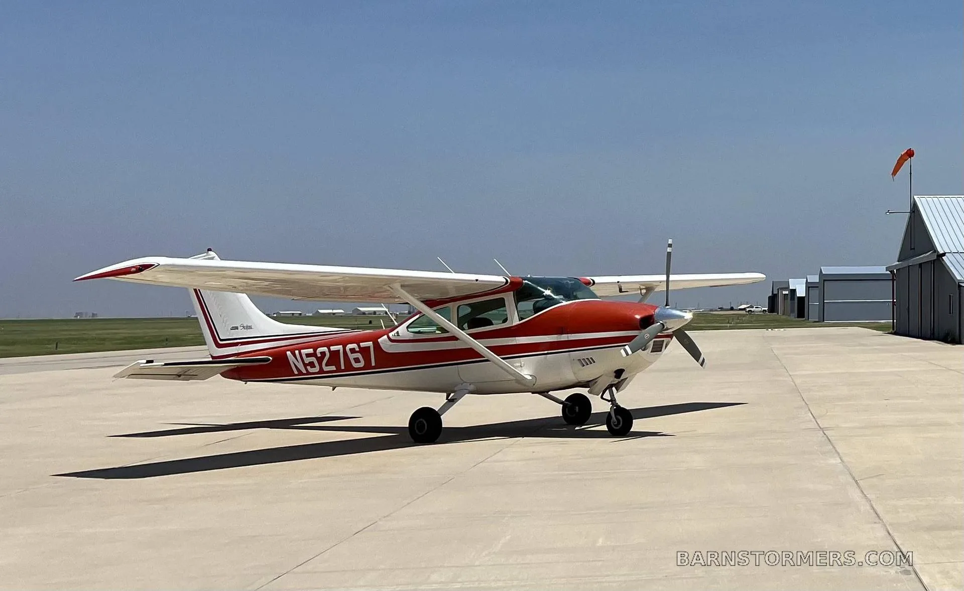 A red and white Cessna 182 Skylane aircraft with registration N52767 is parked on a tarmac under a clear blue sky.