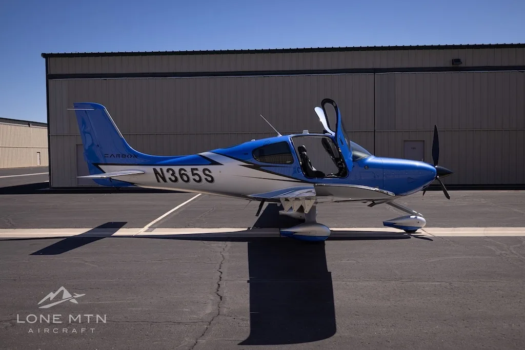 A side view of the blue and silver Cirrus SR22 aircraft, N365S, with its doors open, parked on an asphalt ramp.