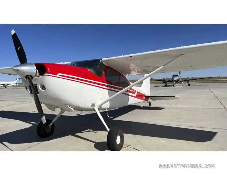 A white and red single-engine propeller aircraft (N42100) on an airport tarmac with other aircraft in the background.