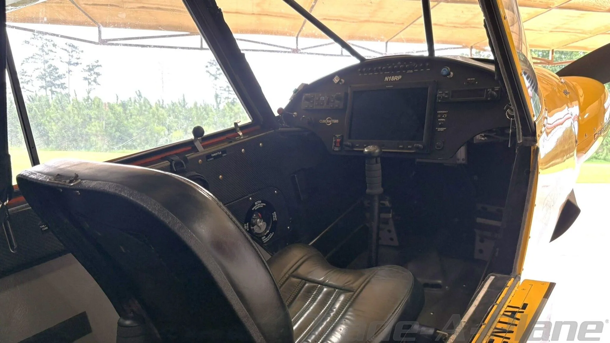 The interior of the CubCrafters Carbon Cub N18RP, showing a black leather seat and the instrument panel from a side angle.
