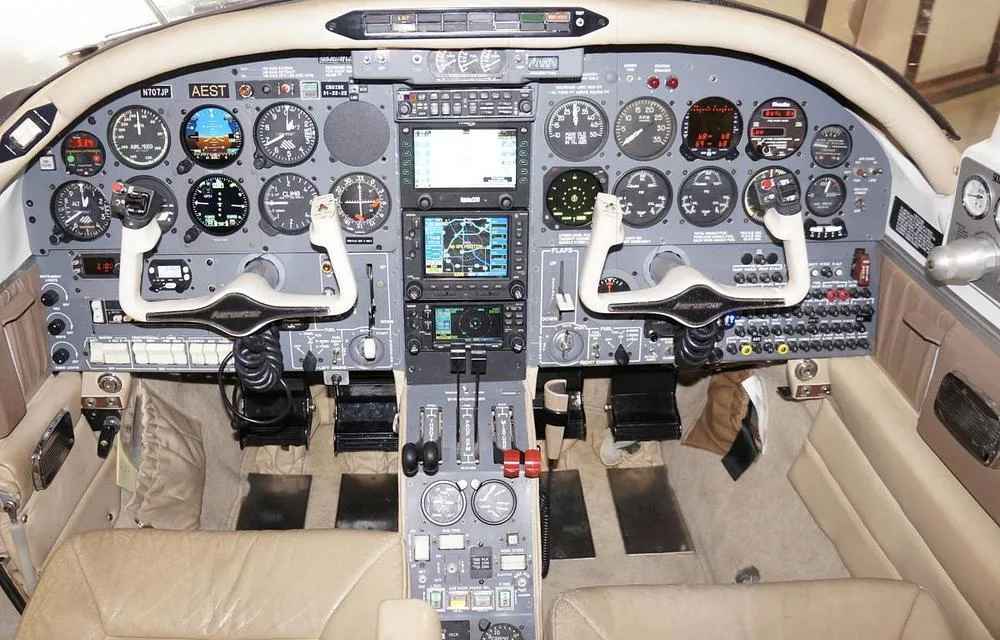 The cockpit of a twin-engine aircraft, featuring a complex array of analog gauges, digital displays, and dual control yokes.