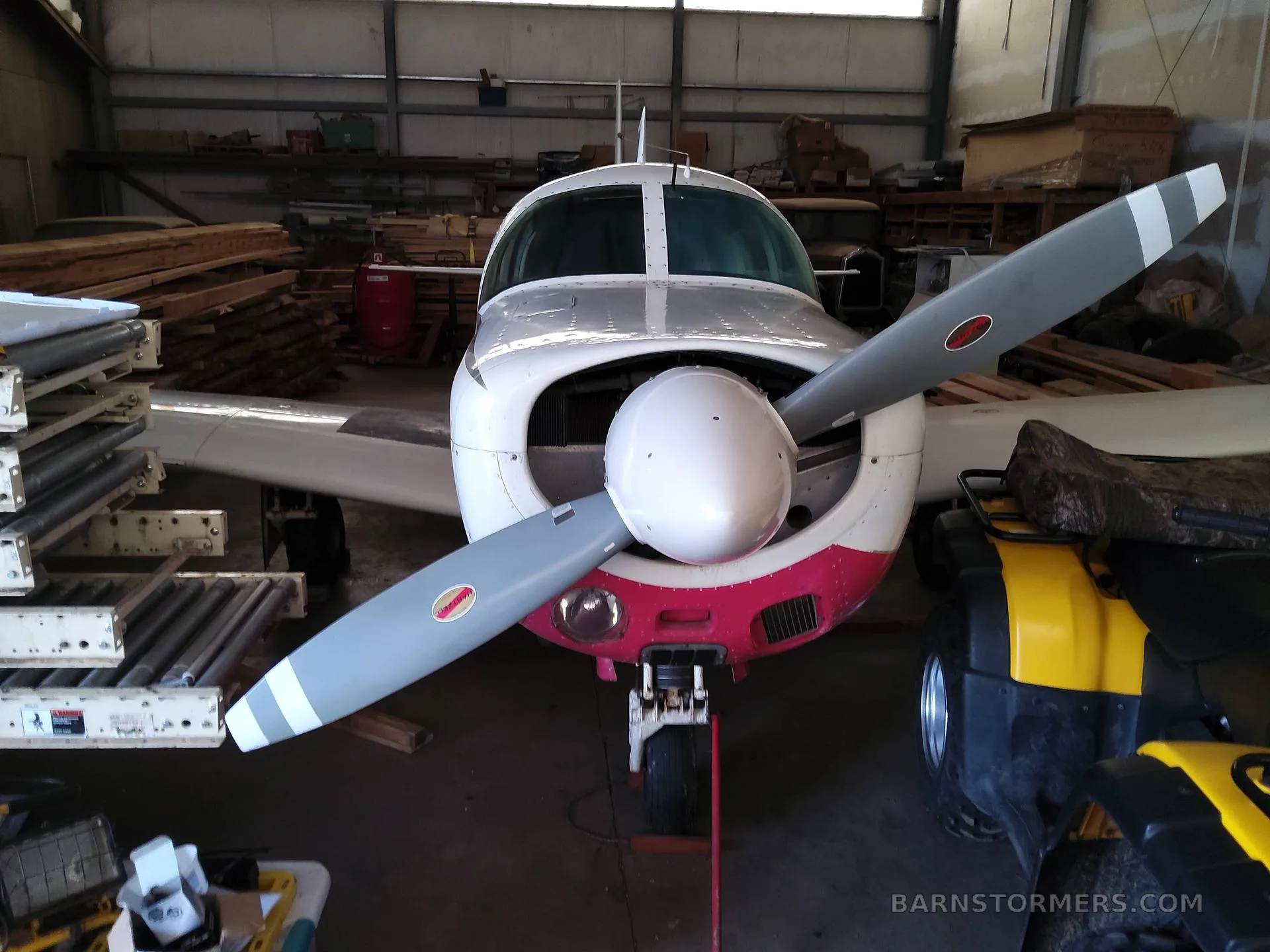 Front view of a white and red single-engine propeller aircraft with its cowling open, parked in a hangar.