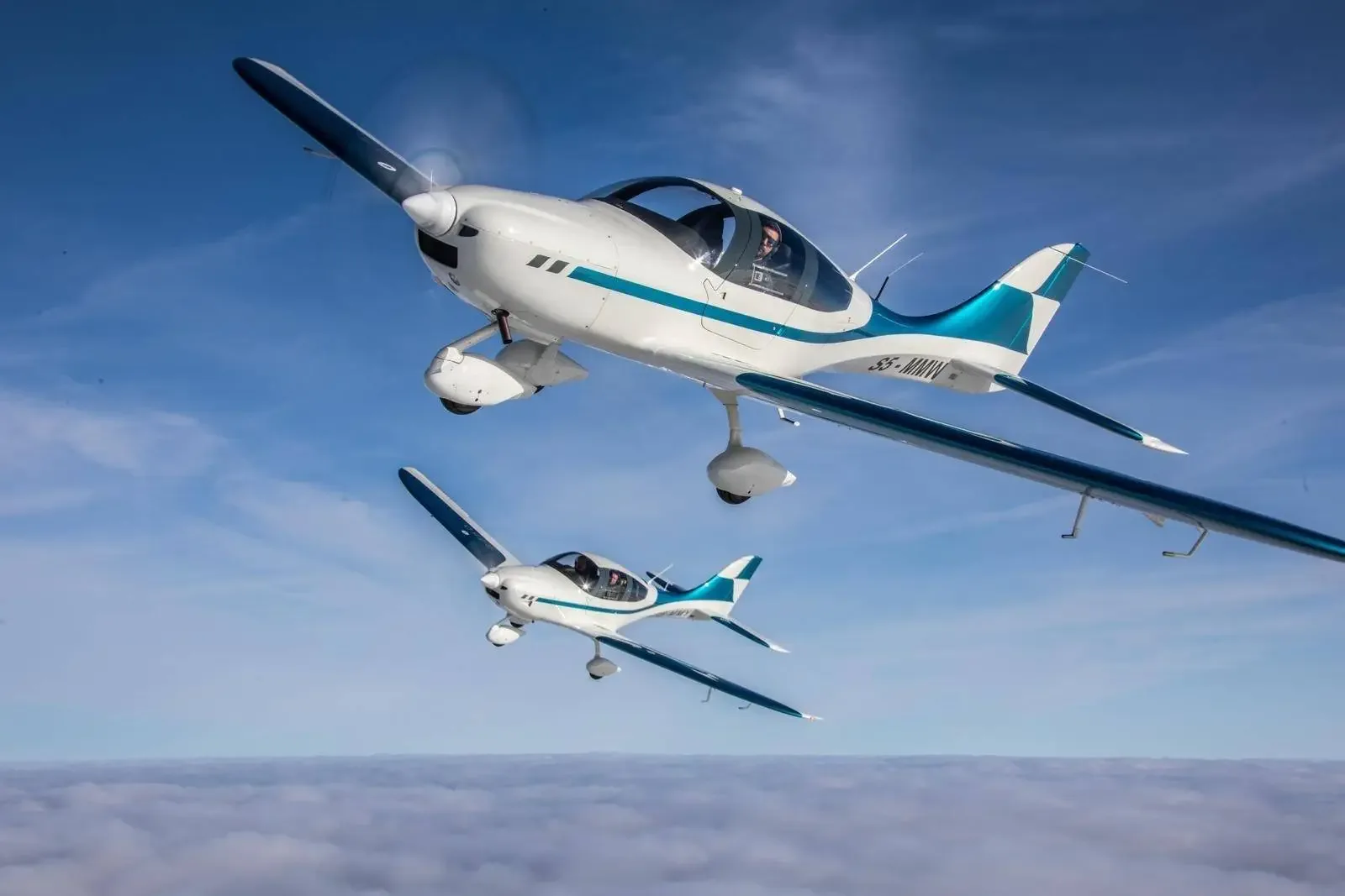 Two white and teal light aircraft with propellers fly in formation against a clear blue sky.