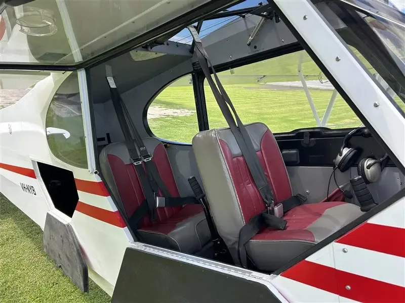 The interior cabin of the Super Cub, showing two red and grey seats with seatbelts and the open door.