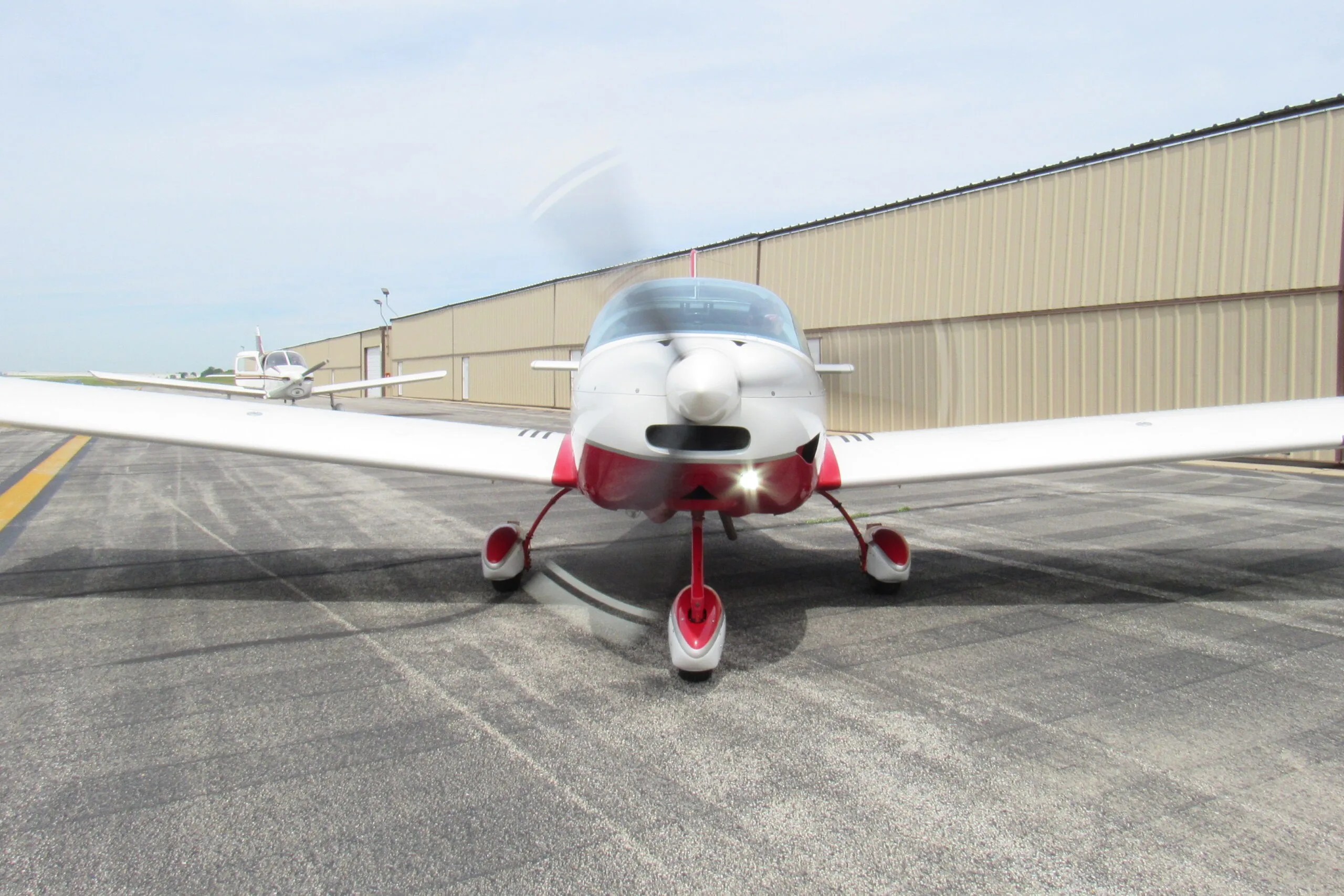 A front view of a white and red SportCruiser aircraft with a spinning propeller on an airport tarmac.