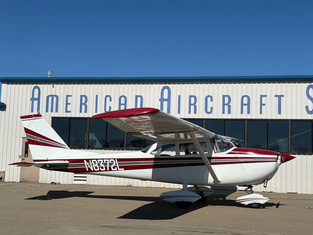 A white and red Cessna 172 Skyhawk aircraft (N8372L) parked on an airfield, viewed from a slightly different angle.