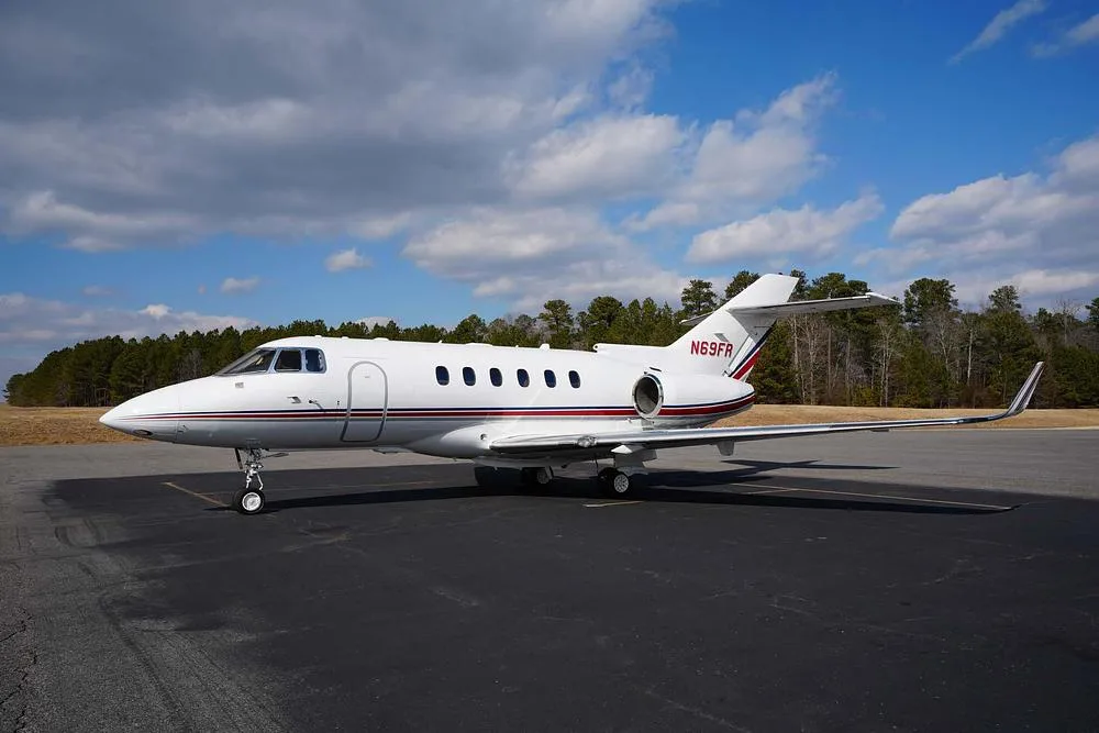 A white business jet with red and blue stripes, registration N69FR, parked on an asphalt tarmac under a partly cloudy sky.