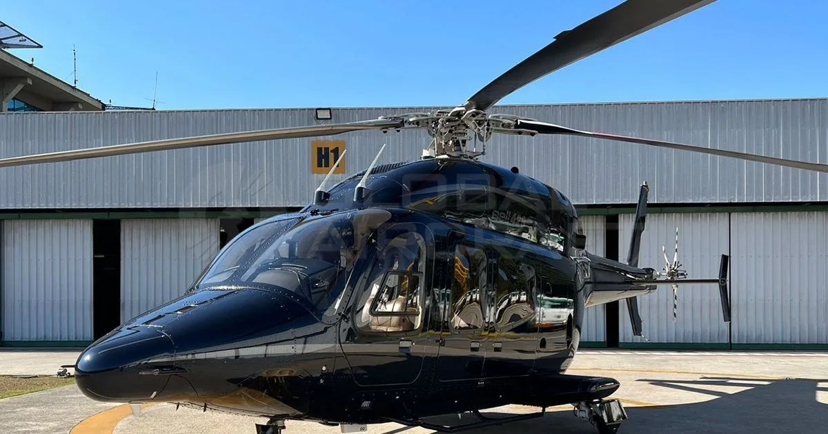 A dark blue Bell 429 helicopter with a glossy finish parked on an airfield, viewed from the front-side.