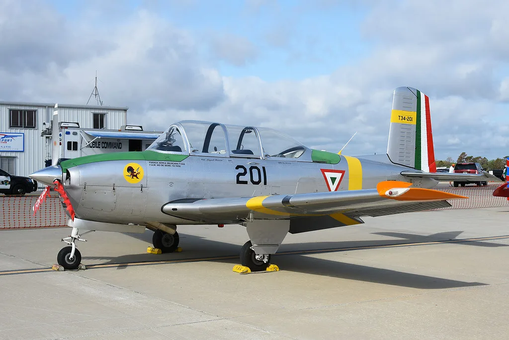 A silver single-engine propeller aircraft with green and yellow trim, and '201' on its side, parked on an airfield.
