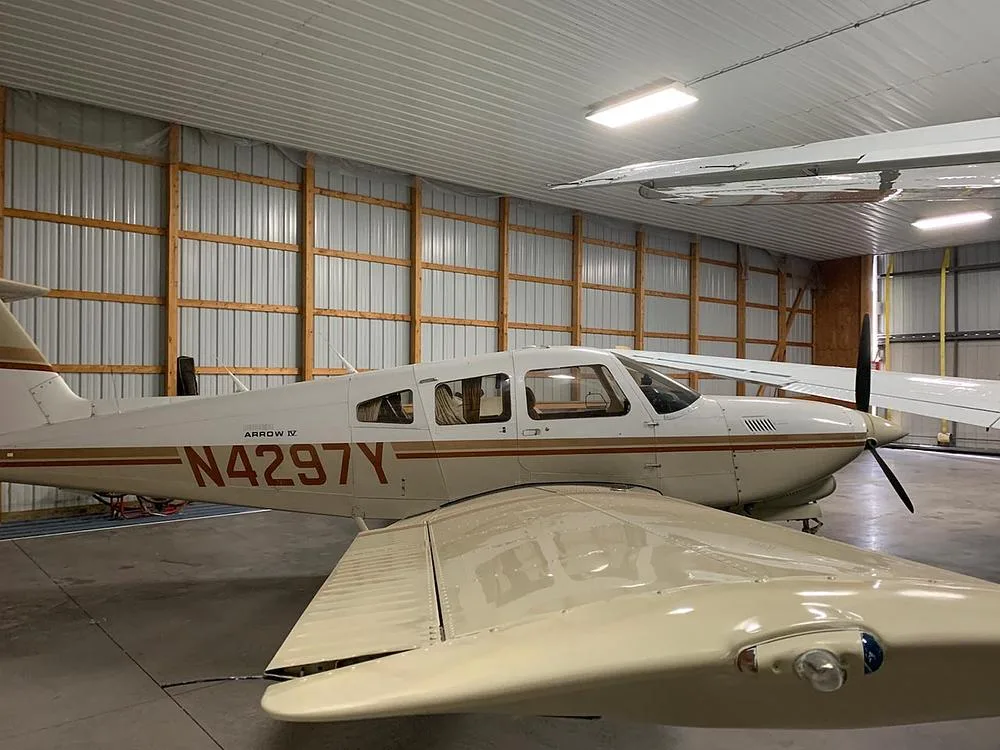 A Piper Arrow IV aircraft, N4297Y, in a white and brown paint scheme, parked inside a hangar.
