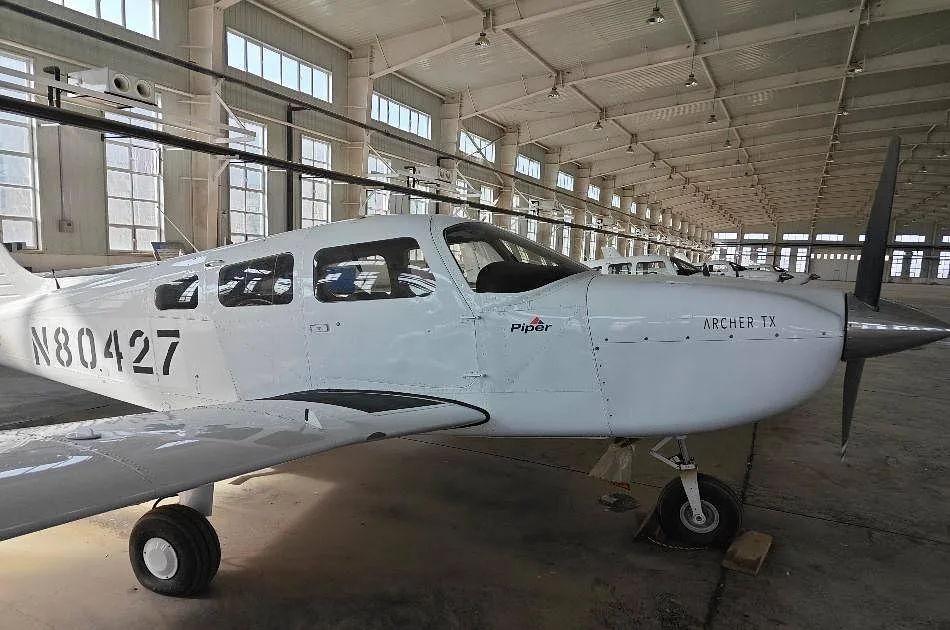 A white Piper Archer TX aircraft with registration N80427 is parked in a hangar, viewed from the front-right.