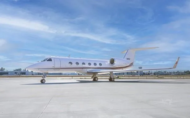 A white Gulfstream business jet with brown stripes is parked on an airport tarmac under a blue sky.