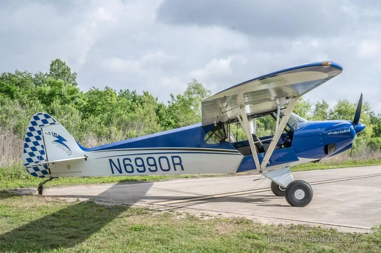 A blue and white single-engine taildragger aircraft (N6990R) with a checkered tail is parked on a concrete pad.