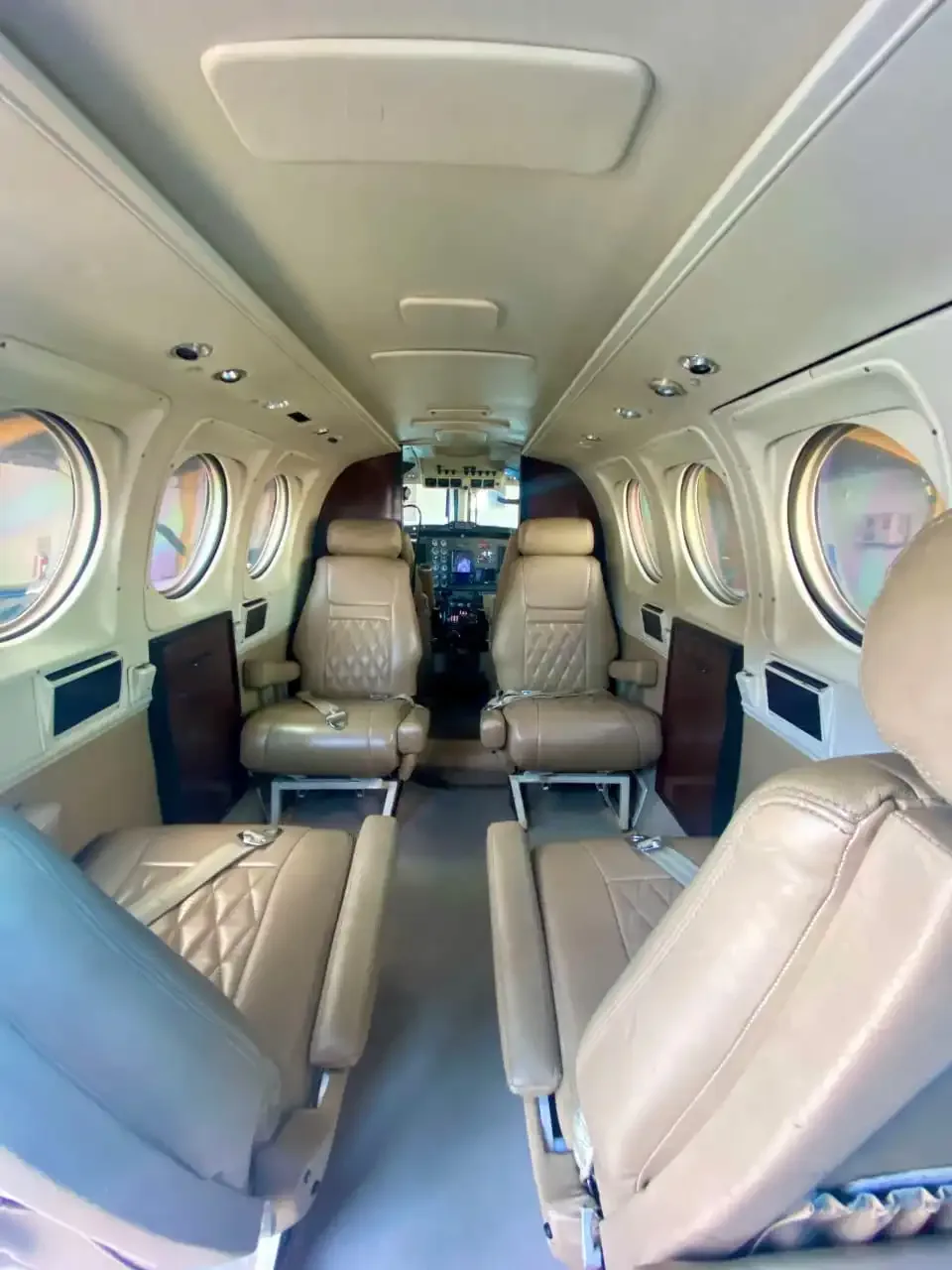 The aircraft cabin interior with tan leather seats and tables, viewed from the rear.
