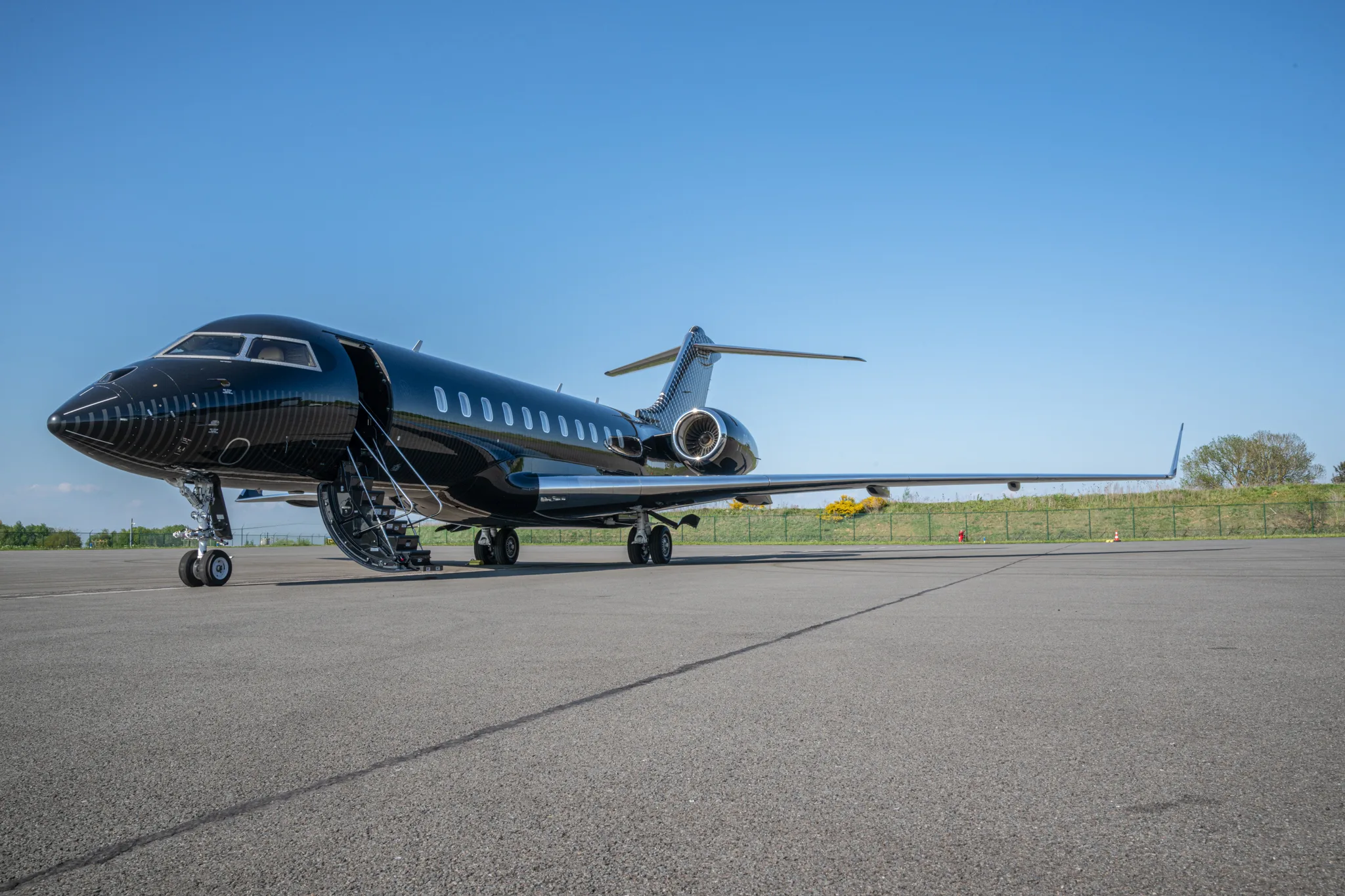 A glossy black business jet is parked on a tarmac with its main door open, under a clear blue sky.