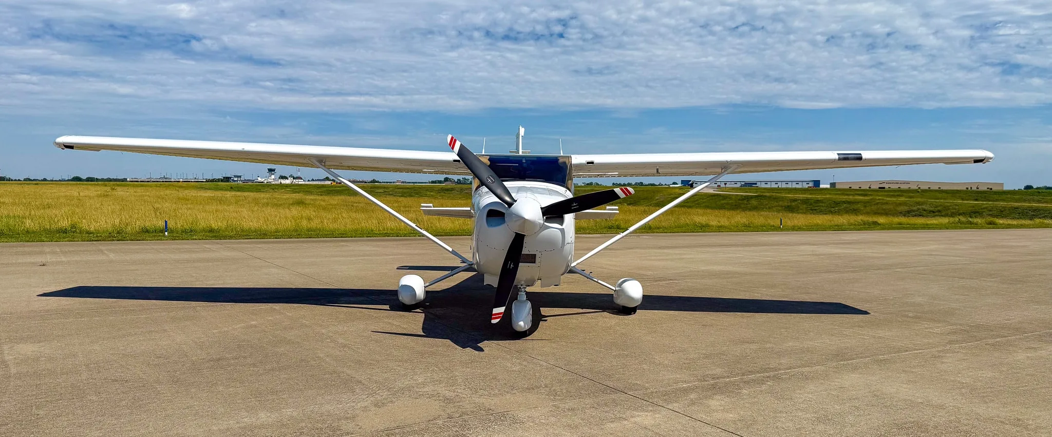 Head-on view of a white Cessna 182 Skylane with red and gray stripes, registration N624CF, parked on an asphalt ramp.