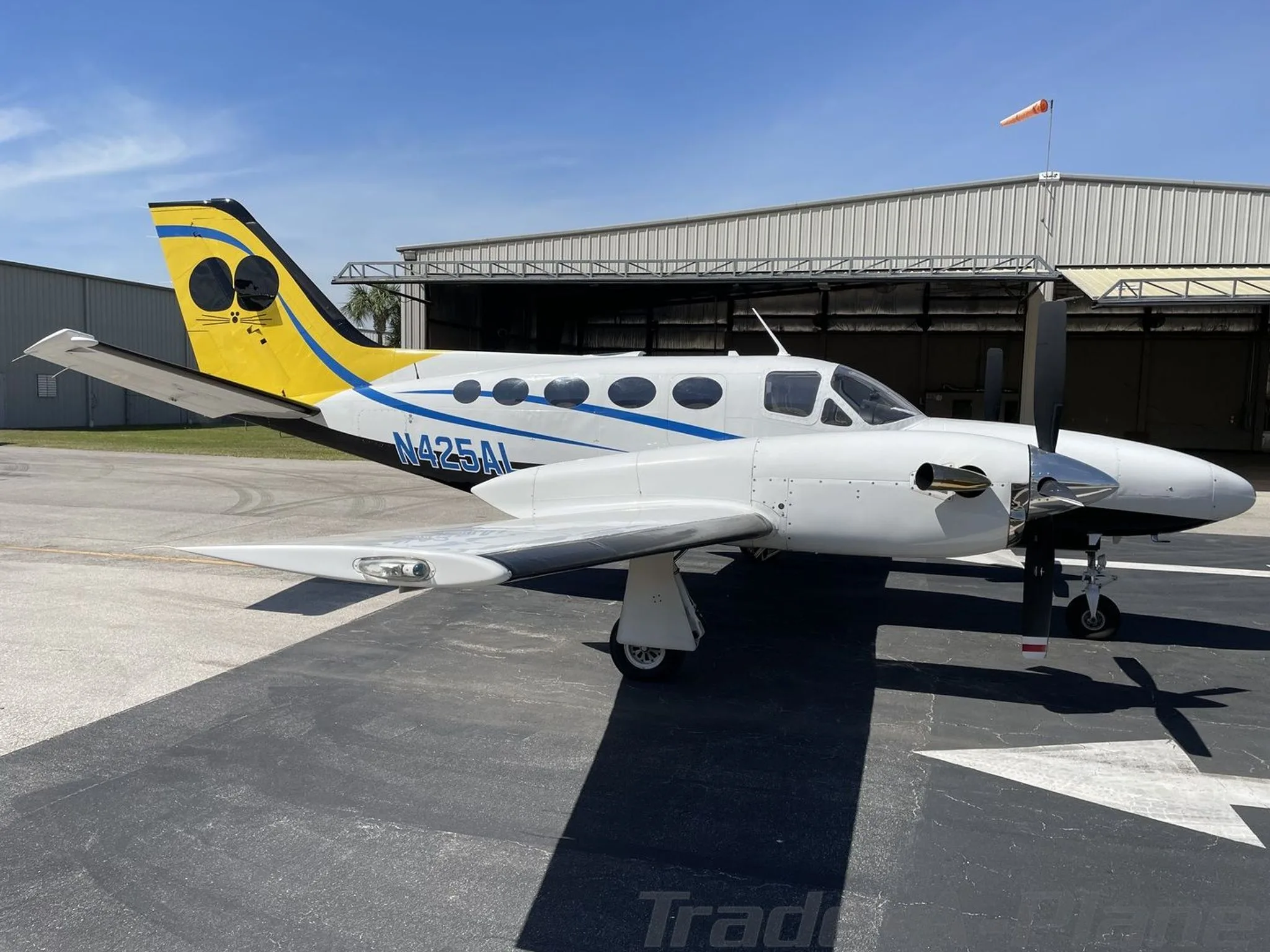 A left side view of the white and blue Cessna 441 Conquest II (N425AL) with a yellow and black tail, parked on a tarmac.