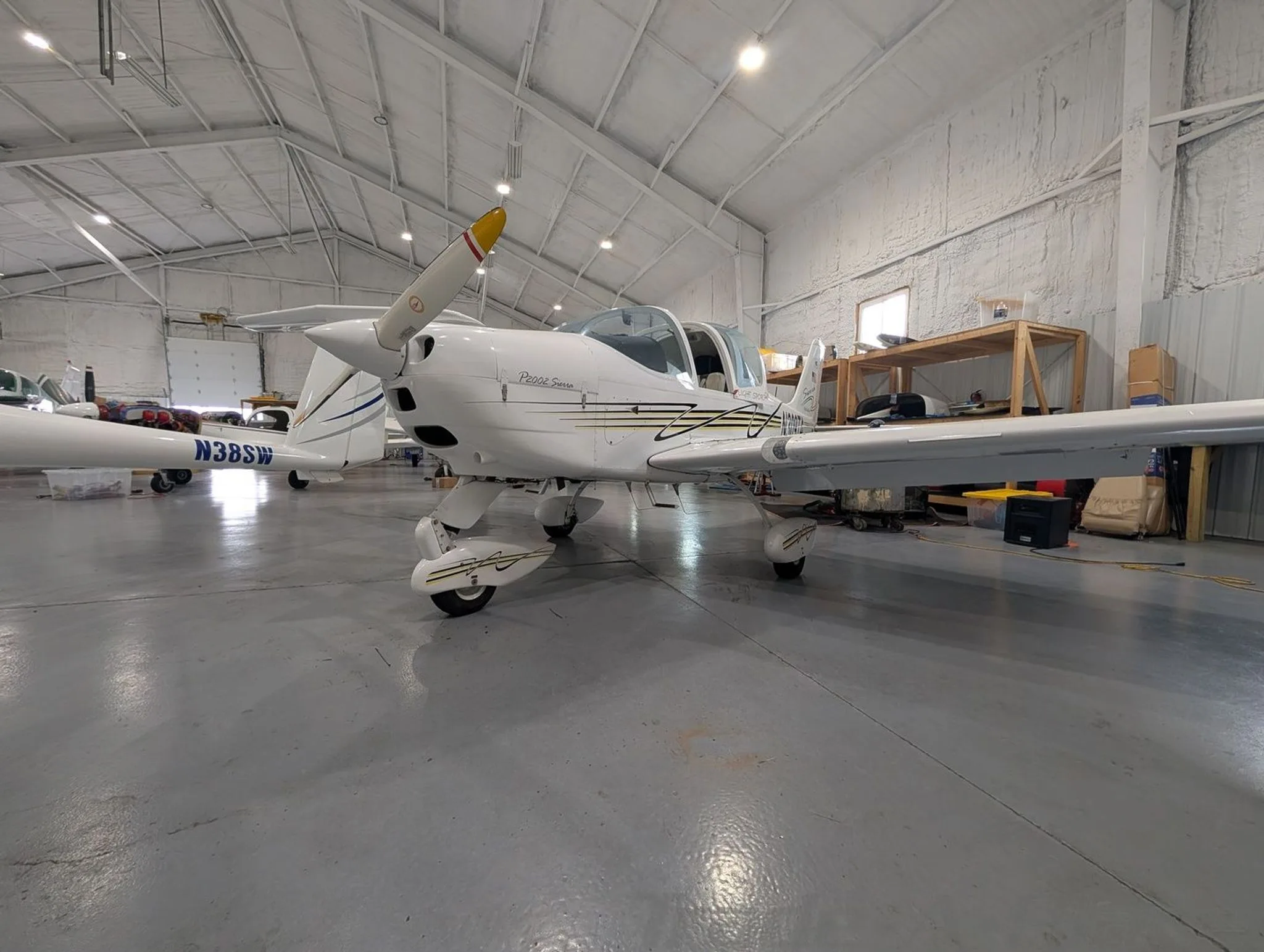 A front view of the white Tecnam P2002 Sierra aircraft with a yellow-tipped propeller, parked in a hangar.