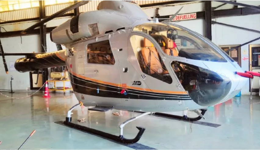 A silver and black MD helicopter with orange stripes is parked inside a hangar.