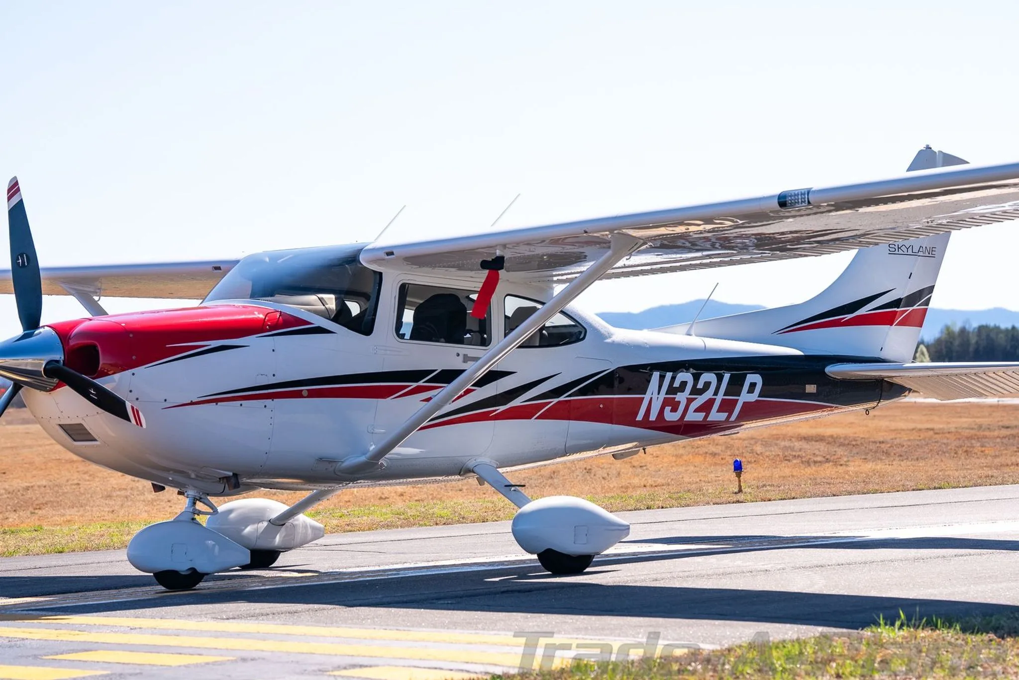 A white Cessna Skylane N32LP with red and black accents on the tarmac, viewed from the front left.