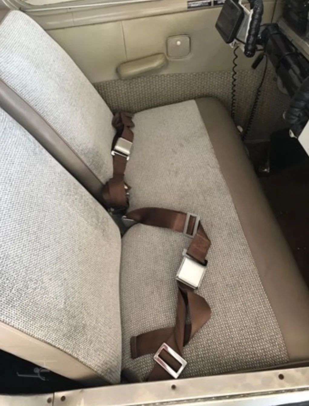 The front passenger seats of the aircraft cabin, featuring brown seatbelts and patterned fabric.