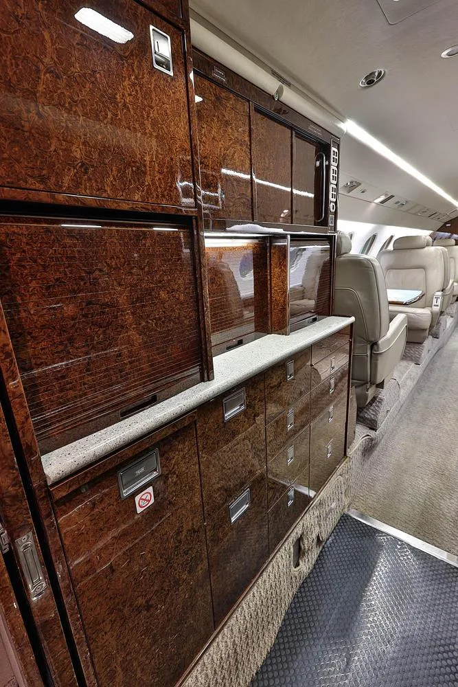 The galley area of a business jet, featuring dark wood cabinetry and a light-colored countertop.