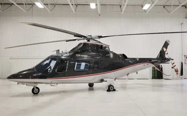 A black and white Agusta A109 Power helicopter with red pinstripes, parked in a well-lit hangar.