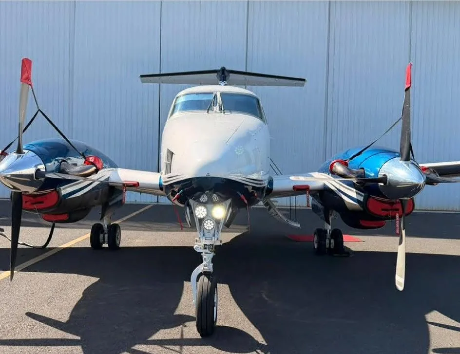 A head-on view of a Beechcraft King Air with blue and white livery, registration ZP-JYA, showing its nose, landing lights, and propellers.