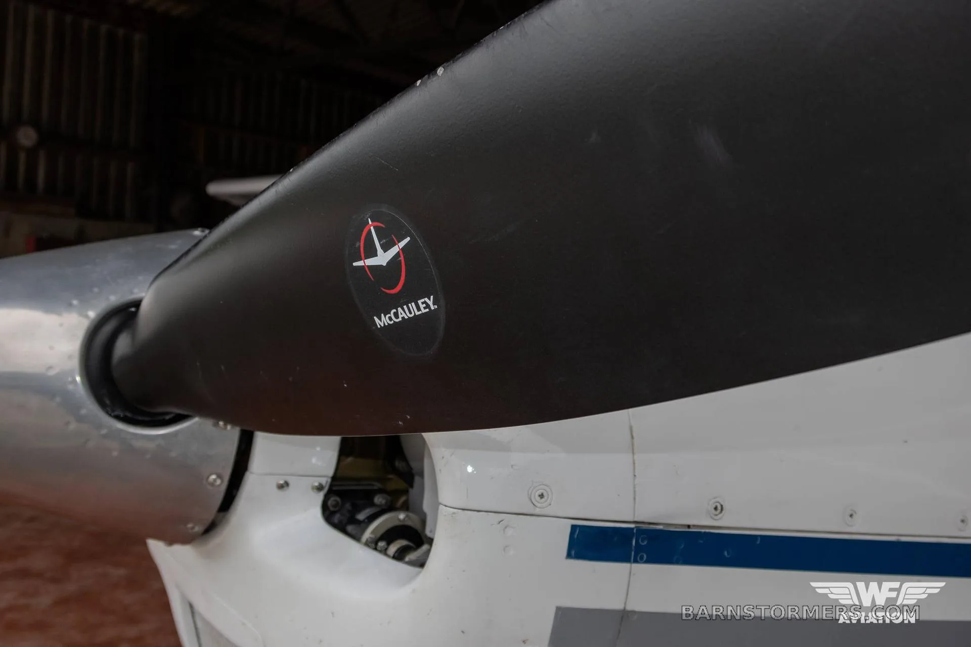 A close-up view of a black McCauley propeller and the white engine cowling of an aircraft.