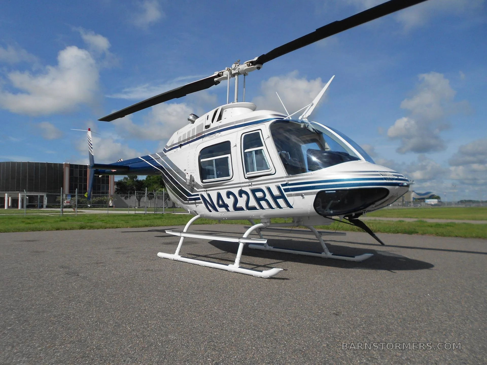 A white and blue Bell 206 helicopter (N422RH) parked on an asphalt apron under a partly cloudy sky.