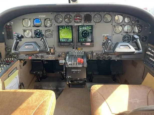 The cockpit instrument panel of an aircraft, featuring analog gauges, two modern glass displays, and dual control yokes.