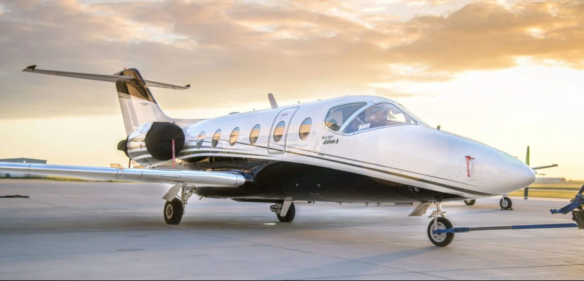 A white and black Beechjet 400A business jet is being towed on an airfield at sunset.
