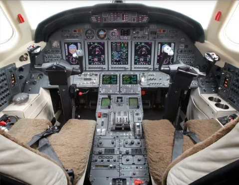 The cockpit of a business jet features multiple digital displays and a complex array of controls.