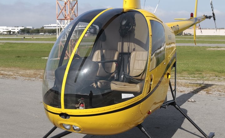 Tail rotor and tail of a yellow Robinson R22 helicopter with a white helicopter in the background.