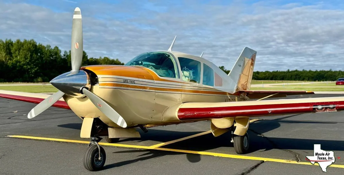 A beige and gold Super Viking aircraft with red accents is parked on an asphalt runway under a partly cloudy sky.
